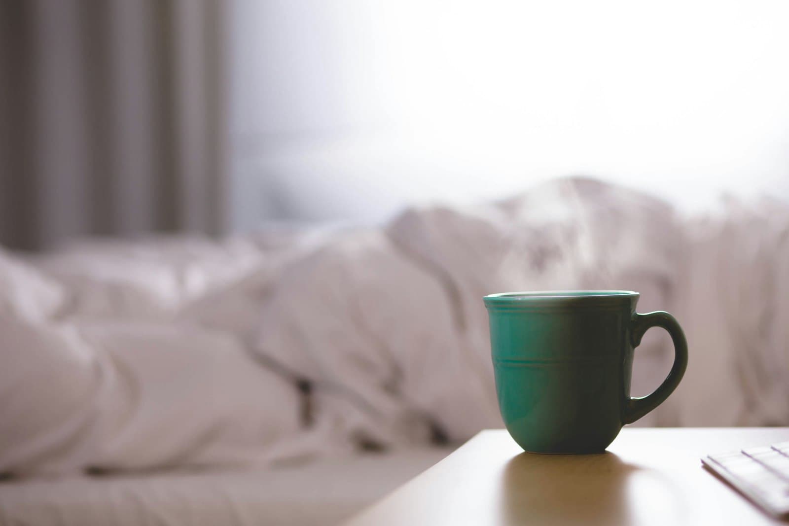 A green mug on a bedside table in soft morning light