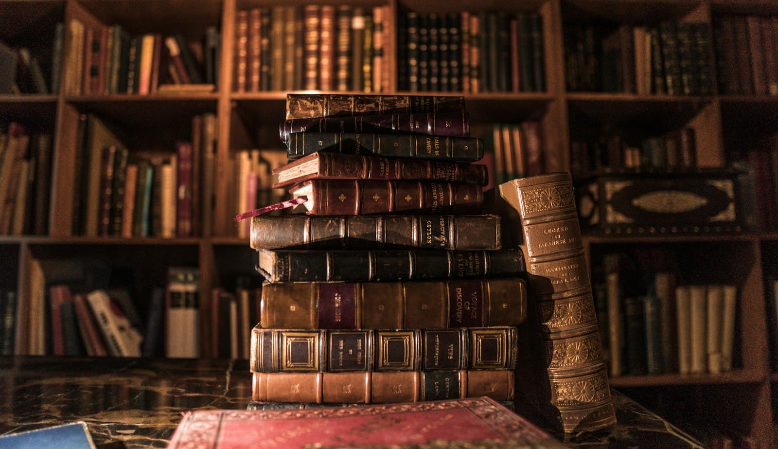 Stack of old leather-bound books in front of a full bookshelf