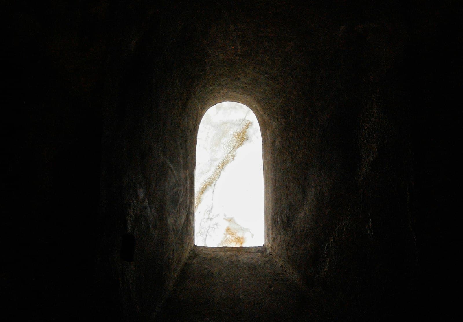 A small arched window of light in a dark stone wall