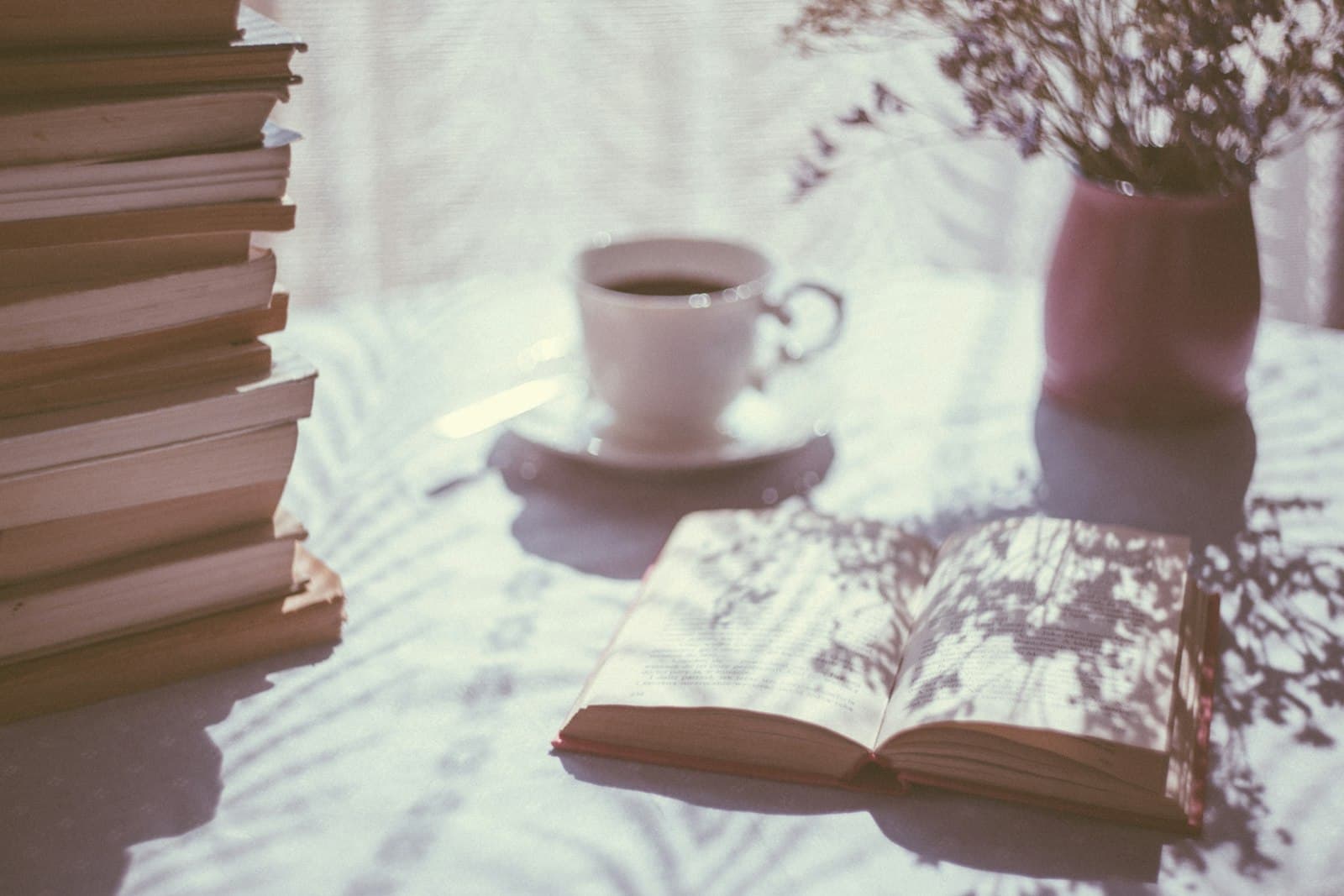 Open book beside a cup of tea on a table in soft window light