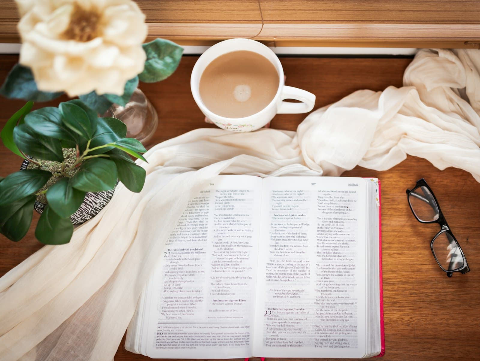 Open book with a cup of coffee, glasses and a plant on a wooden table