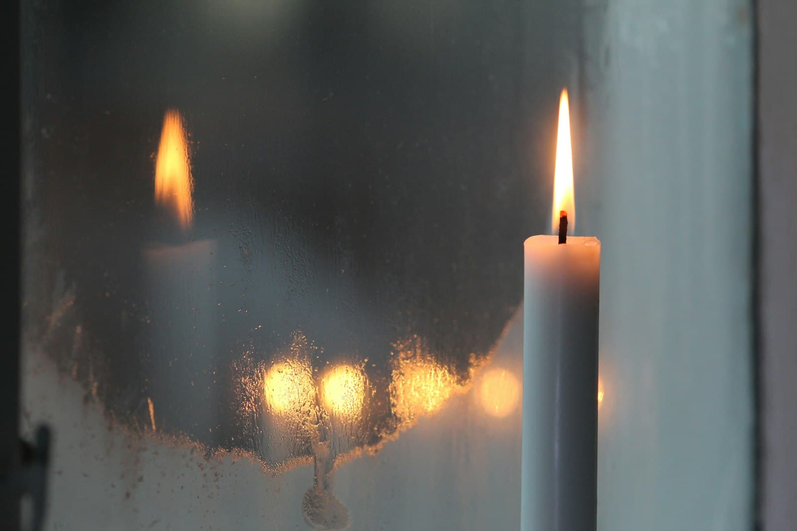A lit white candle beside a rain-streaked window at dusk