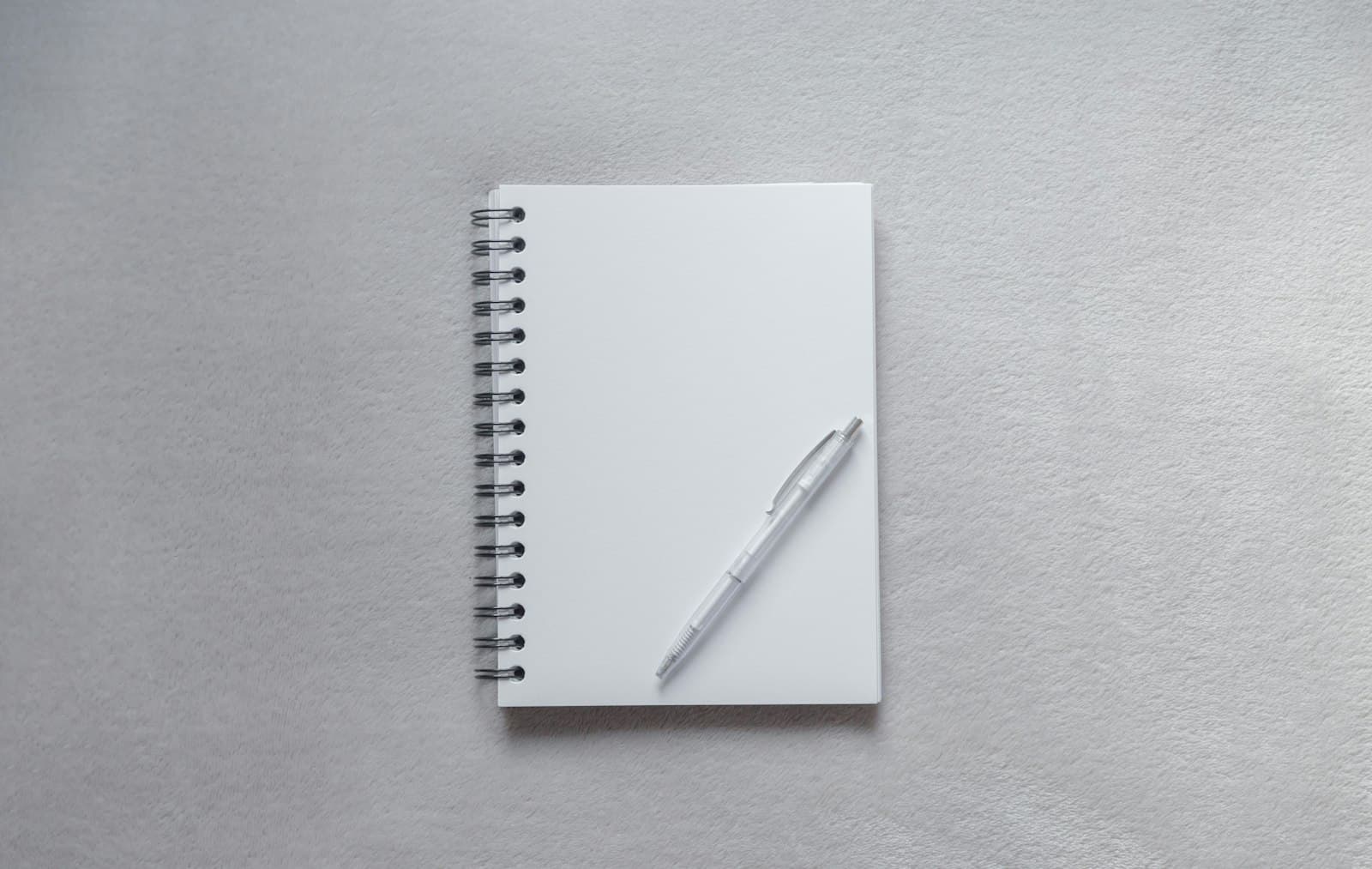 White spiral notebook with a pen on a gray surface