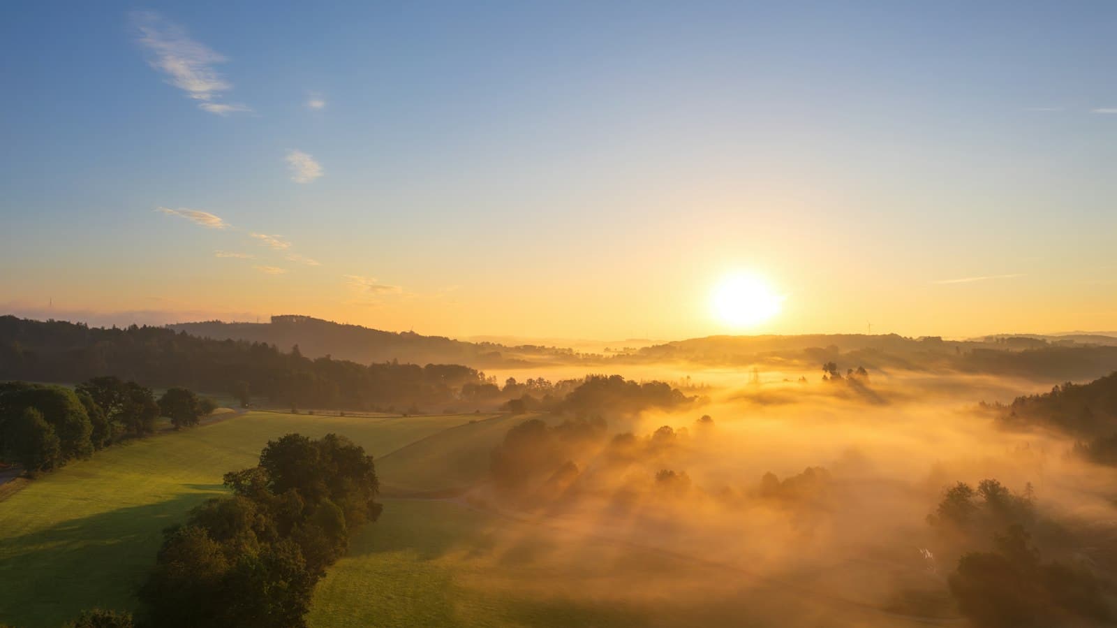 Low golden sun over rolling green hills and a valley filled with mist