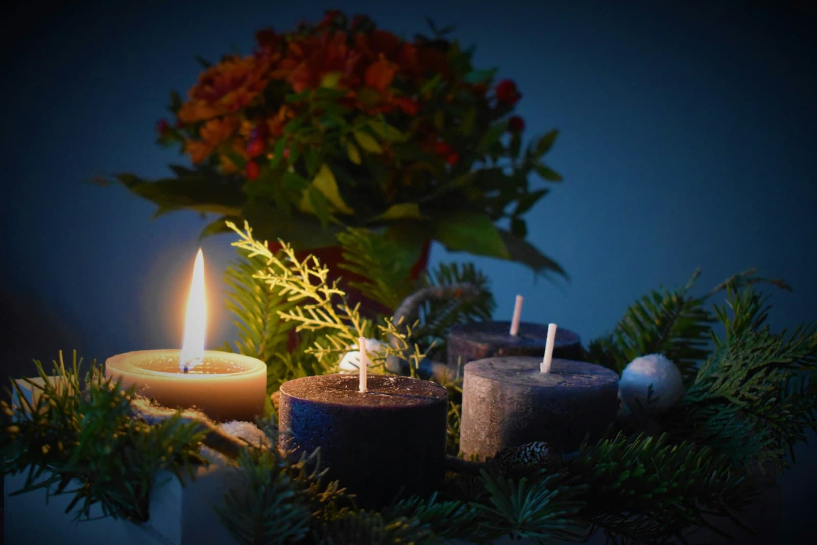 A lit candle beside three unlit candles in an evergreen wreath